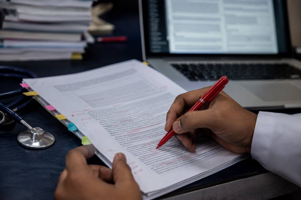 Reviewer annotating a research manuscript with a red pen